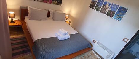 A neatly arranged bedroom with a bed, a ceiling fan, a wall-mounted air conditioner, and a series of framed pictures.