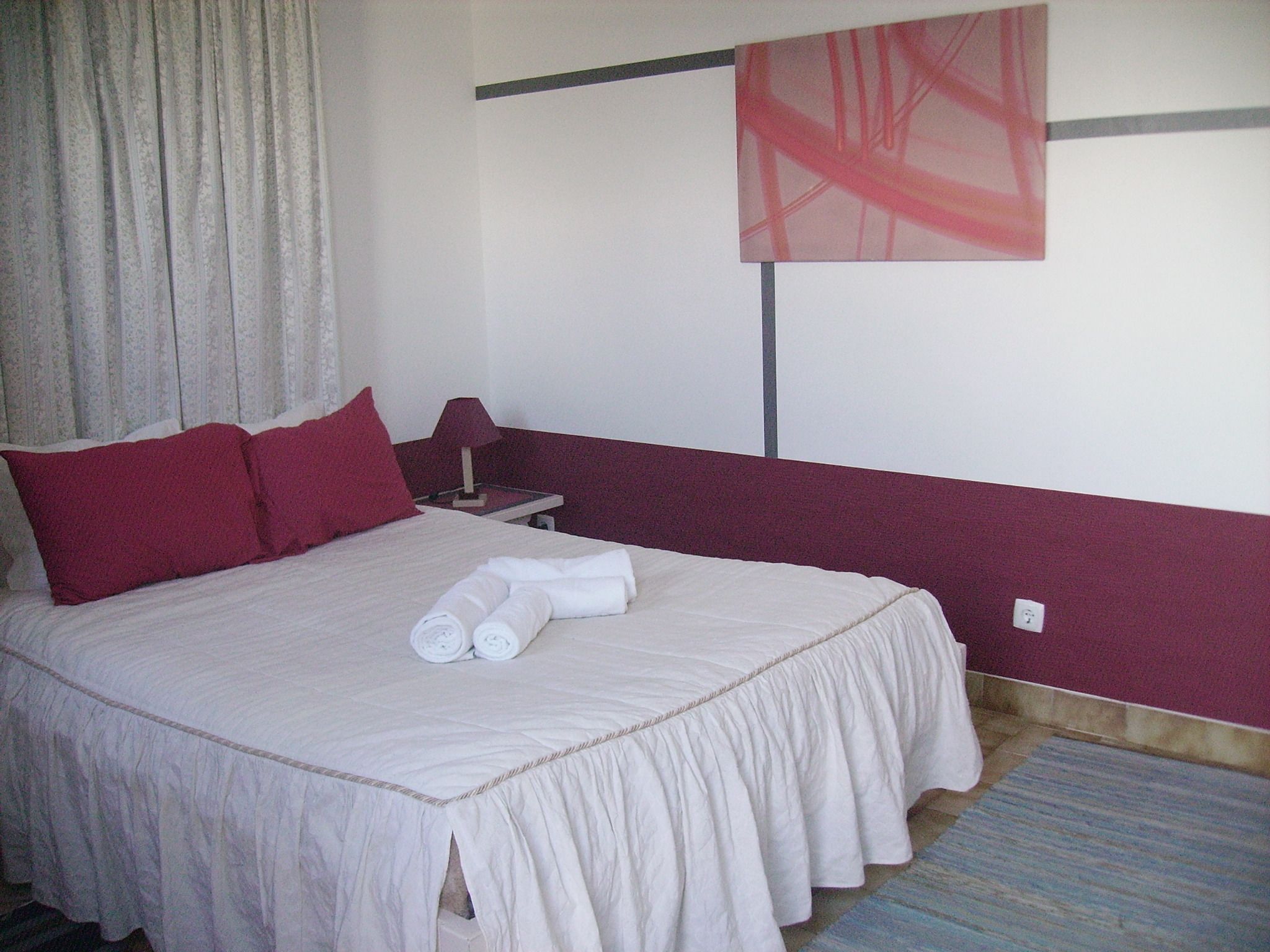 Ein Hotelzimmer mit Bett, Kissen, Nachttisch, Lampe und einem Gemälde an der Wand.