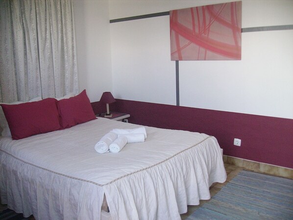 A hotel room with a bed, pillows, a nightstand, a lamp, and a painting on the wall.
