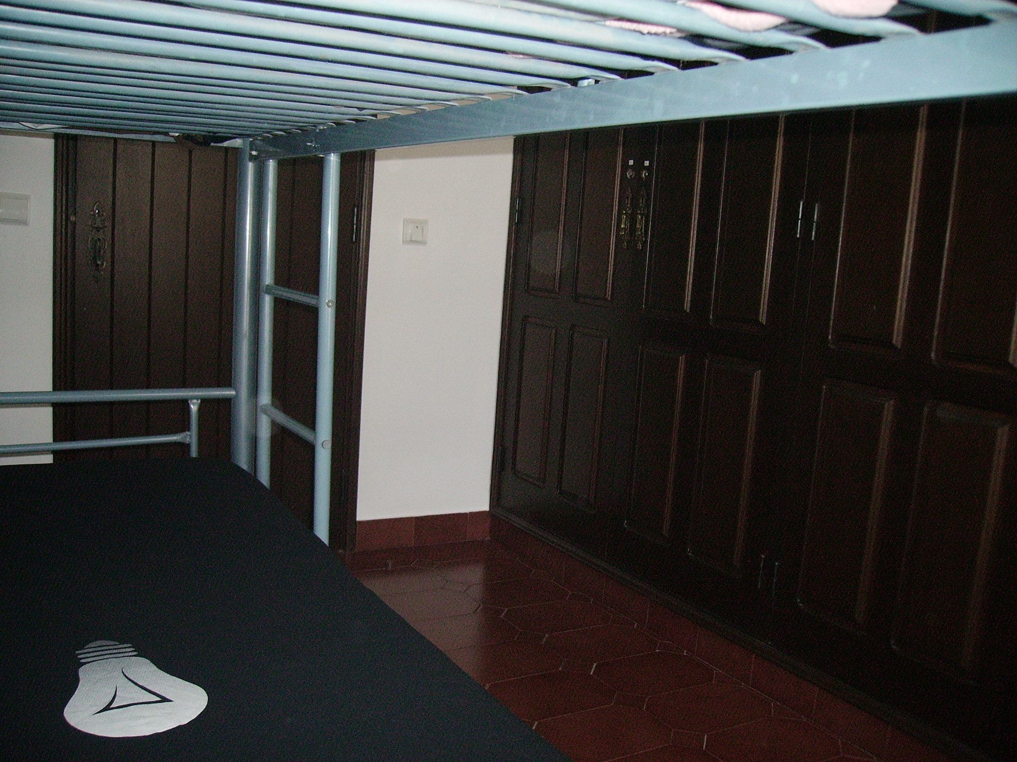 A bunk bed with a metal ladder, a white wall, and a wooden door.