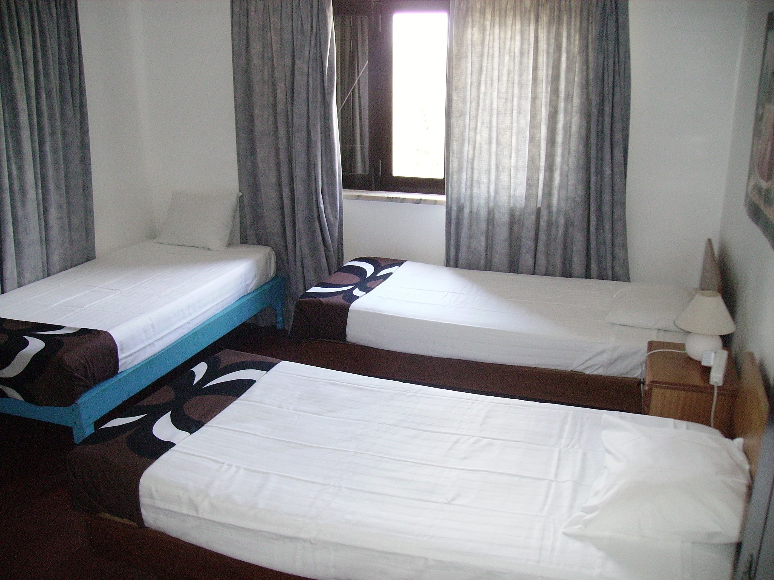 Una habitación de hotel con dos camas individuales, una mesita, una mesita de noche y un ventanal con cortinas.