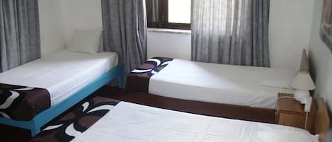 Una habitación de hotel con dos camas individuales, una mesita, una mesita de noche y un ventanal con cortinas.