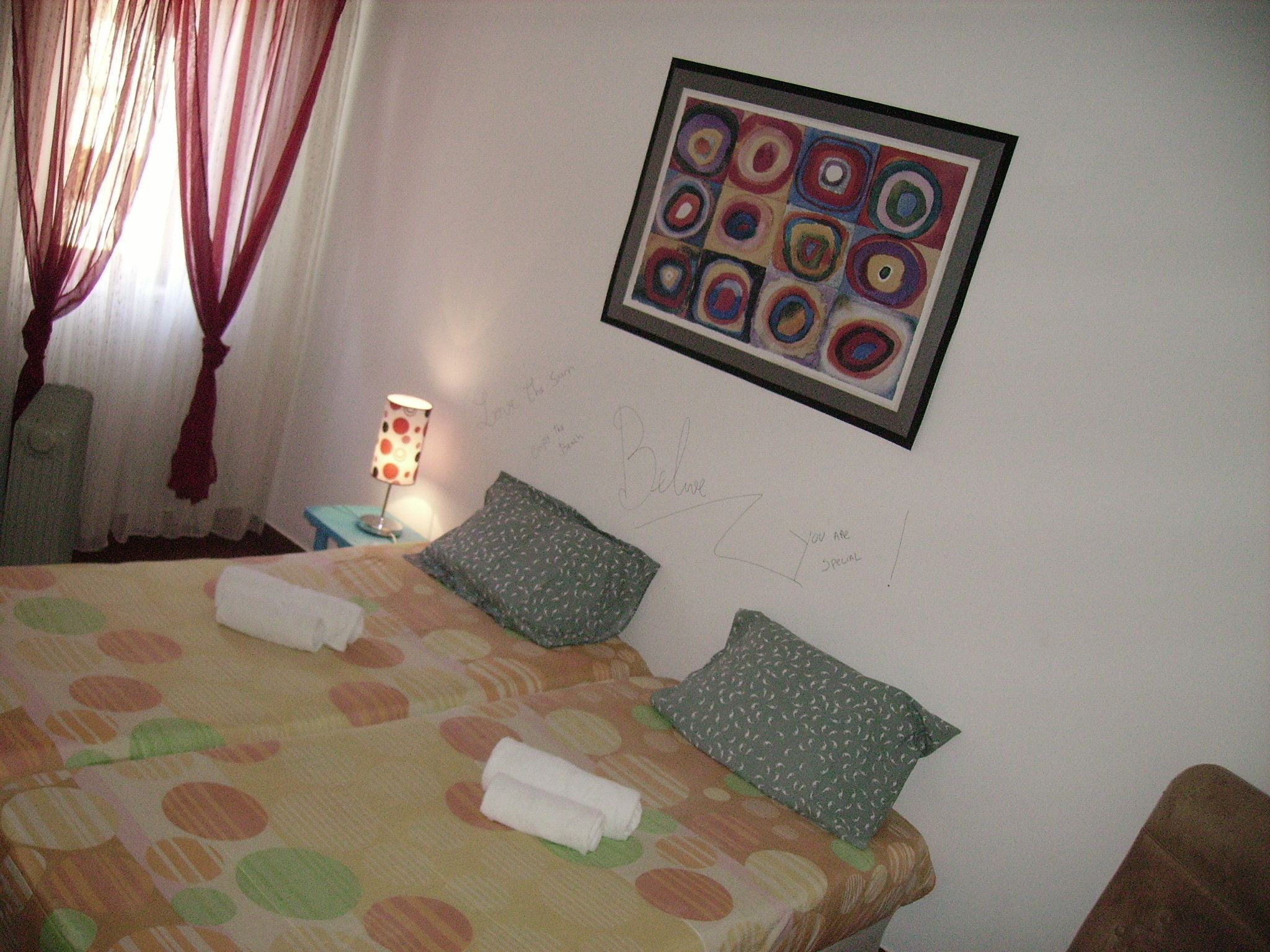 Una camera da letto con un letto, cuscini, un comodino, una lampada e un quadro appeso al muro.