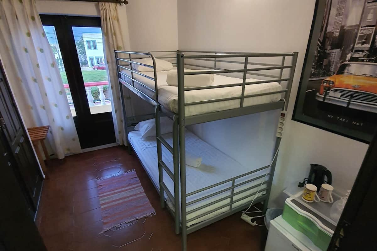 Quarto com beliche e vista para o exterior, pequena cozinha e quadro na parede.
