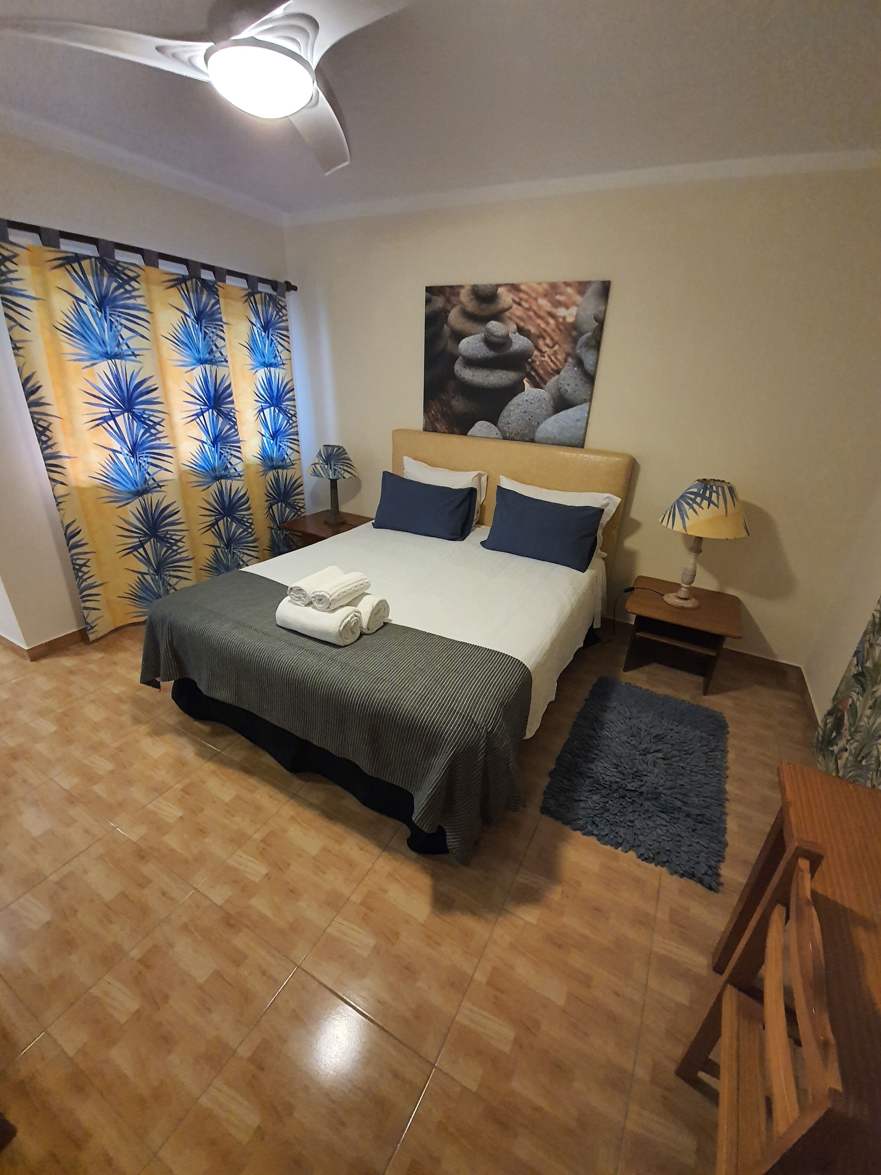 A neatly arranged bedroom with a bed, a bedside table, a lamp, and a painting on the wall.
