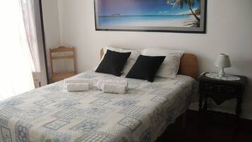 A neatly made bed with a patterned bedspread, two black pillows, and a white pillow. There is a framed picture of a beach scene on the wall above the bed.