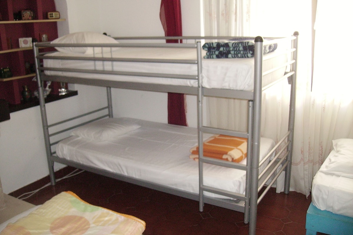 Quarto com beliche, prateleira e janela.