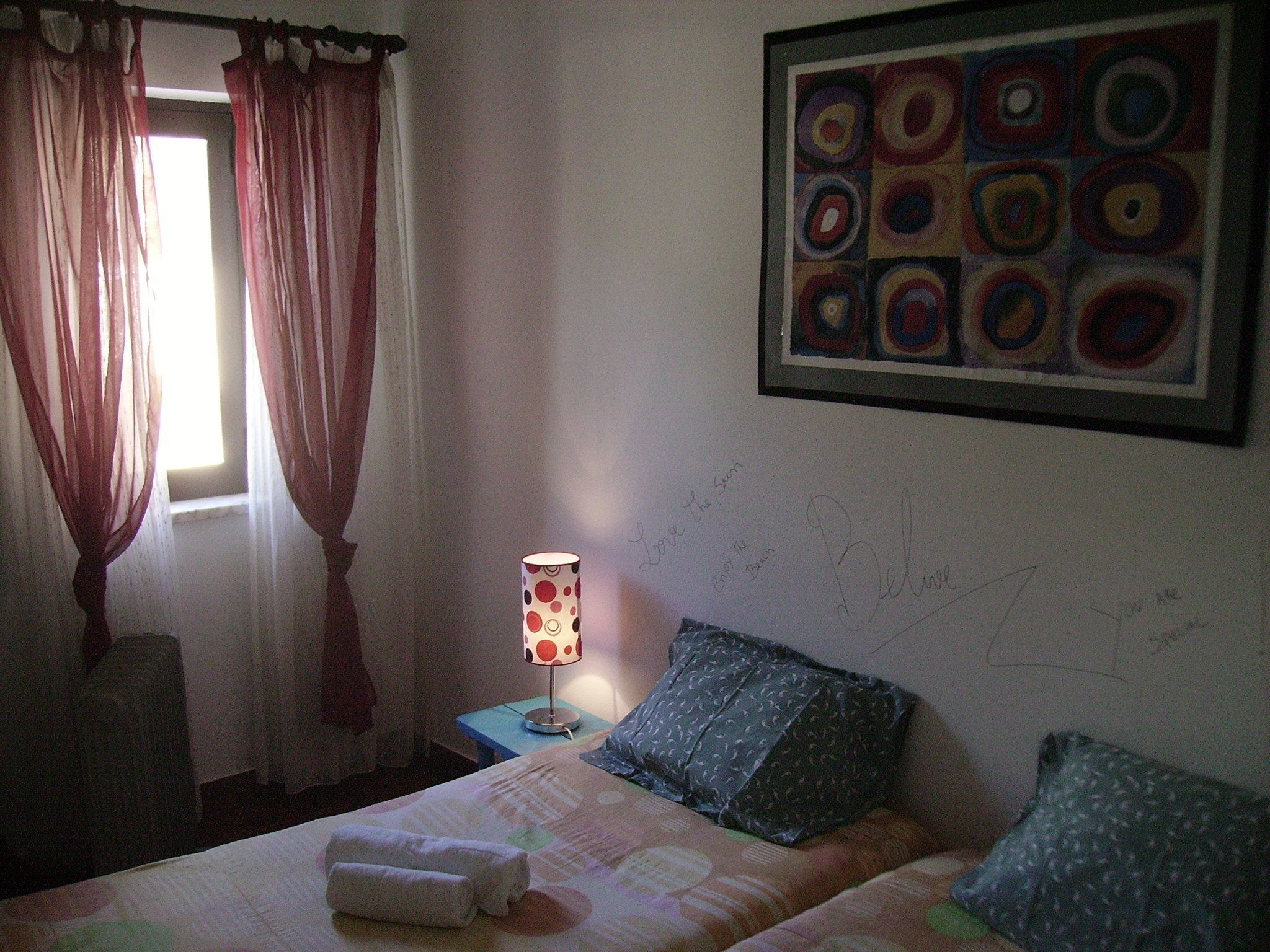 Une chambre d’hôtel avec un lit, une lampe, une fenêtre avec des rideaux et un tableau au mur.