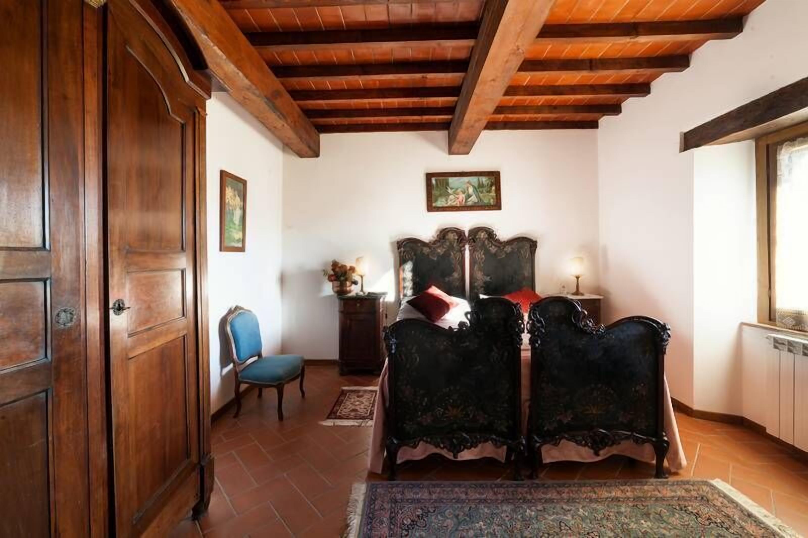 A bedroom with a wooden ceiling, a bed with ornate headboard, a chair, and a nightstand.
