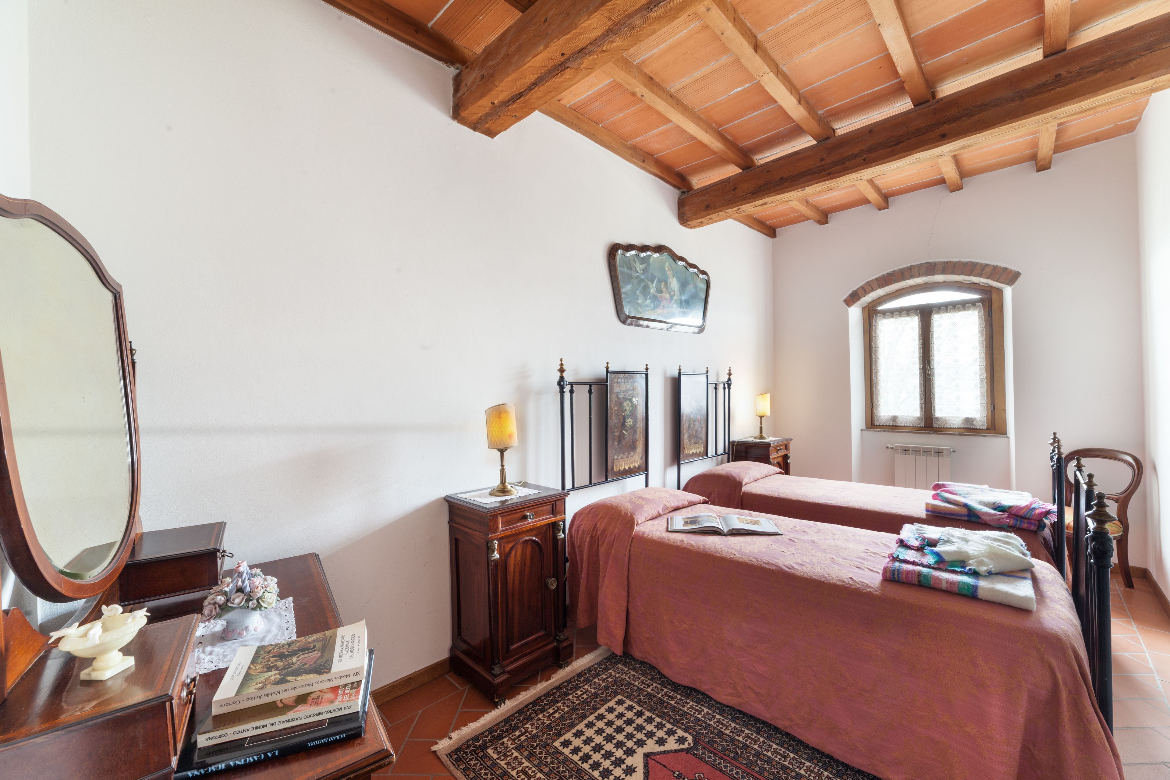 Un dormitorio con dos camas, techo de madera, un espejo, cómoda y ventana.
