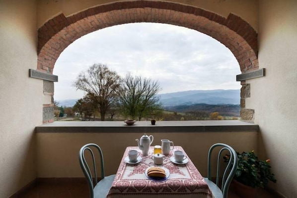 A balcony with a table set for tea, a brick archway, and a view of distant mountains.