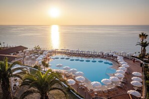 Zona de piscina en un resort con tumbonas y sombrillas, rodeada de palmeras y vistas al mar.