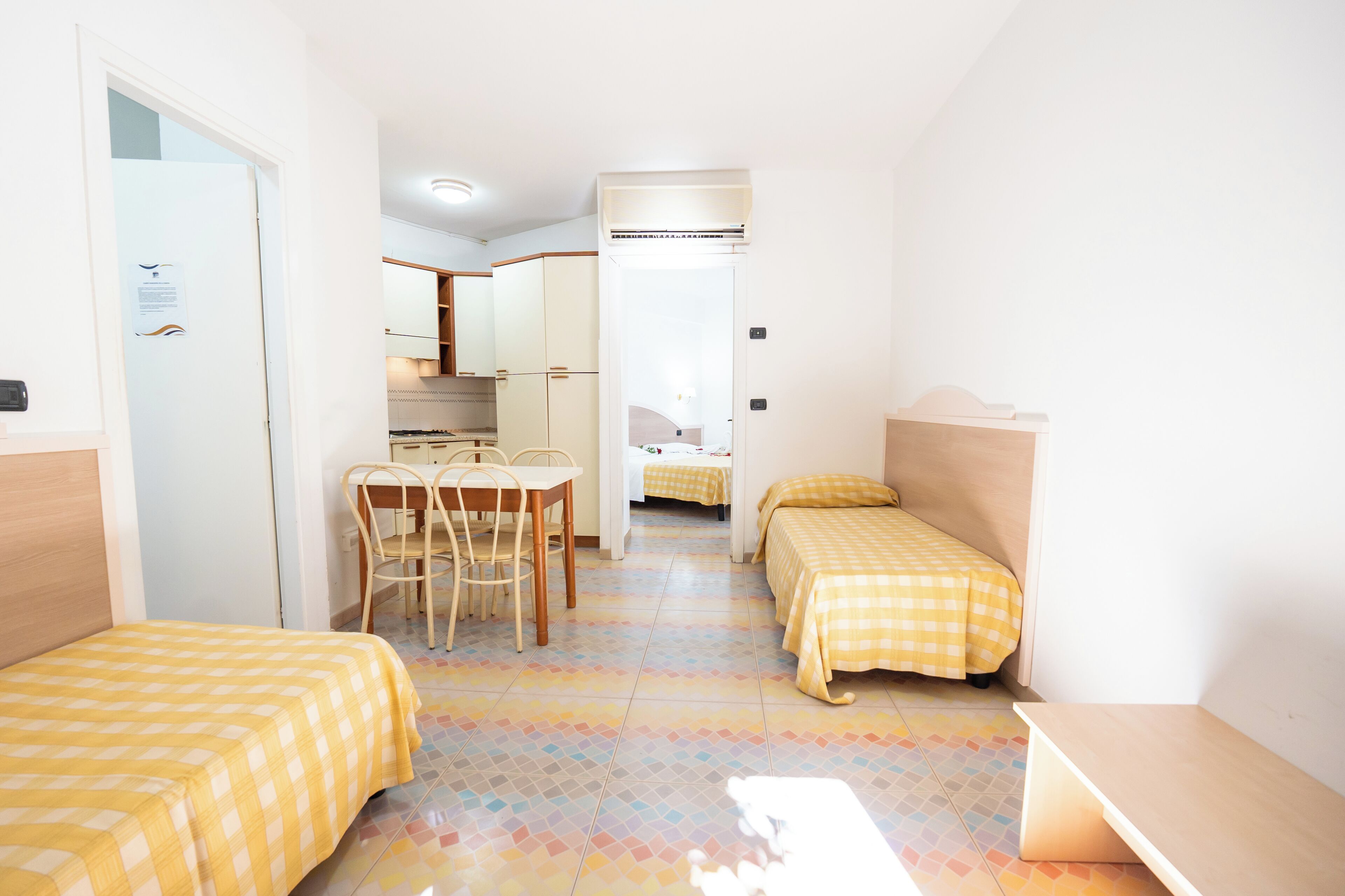 A small, clean room with two beds, a desk, and a chair.