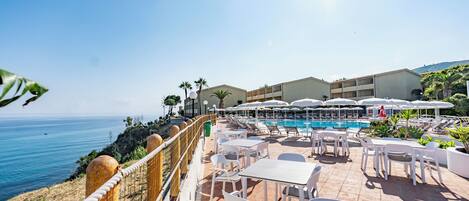 A resort patio with outdoor seating, a pool, and a view of the sea.