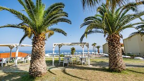 A beachside outdoor seating area with palm trees, white tables, and umbrellas. - Poggio di Tropea (Parghelia)
