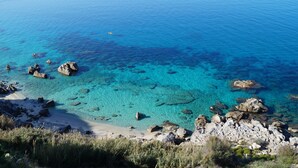 A coastal landscape with clear turquoise waters, rocky shorelines, and sparse vegetation. - Poggio di Tropea (Parghelia)