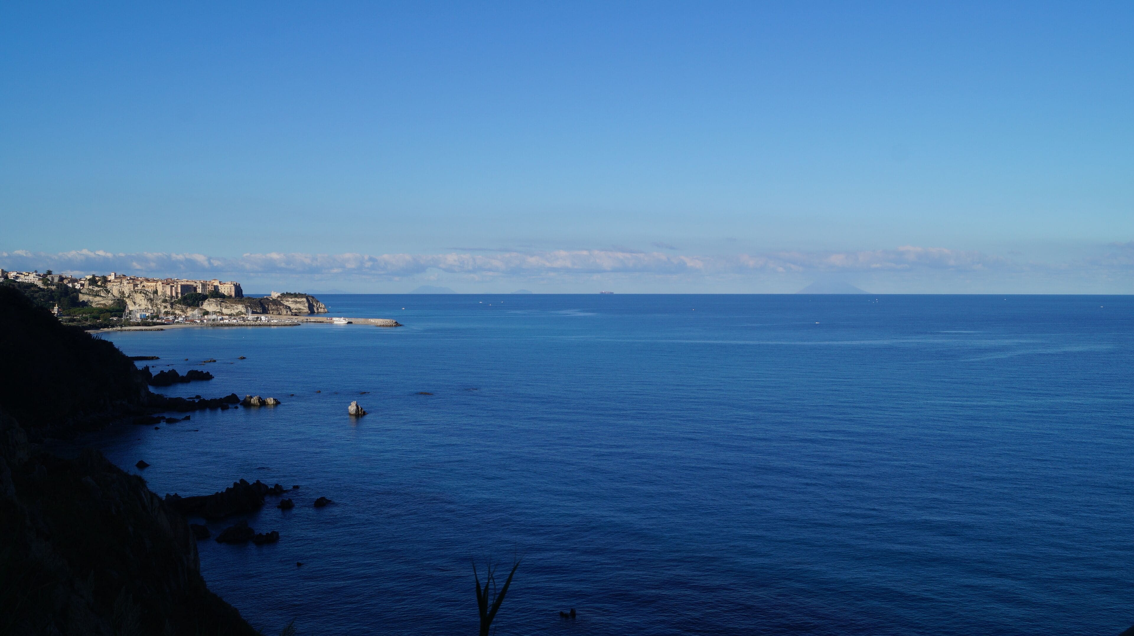 A coastal view with a rocky shoreline, a town with historic buildings, and calm sea.