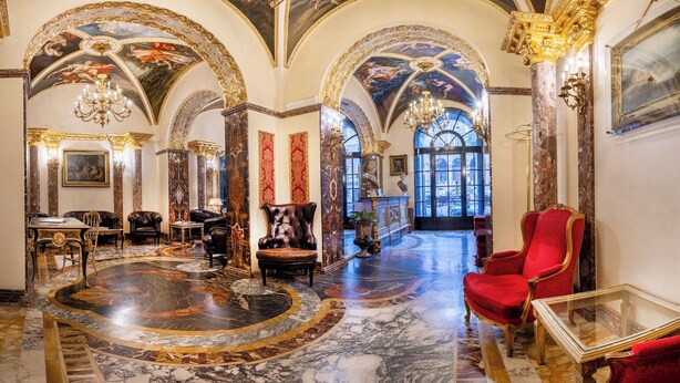 Un intérieur luxueux avec des sols en marbre, des meubles richement décorés et de hauts plafonds ornés de fresques.