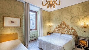 Une chambre d’hôtel avec un grand lit, un lustre, un tableau encadré au mur et une vue sur les immeubles par la fenêtre.