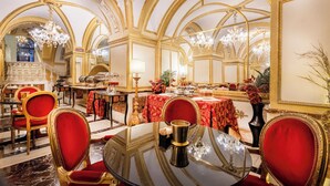 Un espace de restauration luxueux, agrémenté de lustres décoratifs, de chaises à l’assise rouge et d’un buffet.