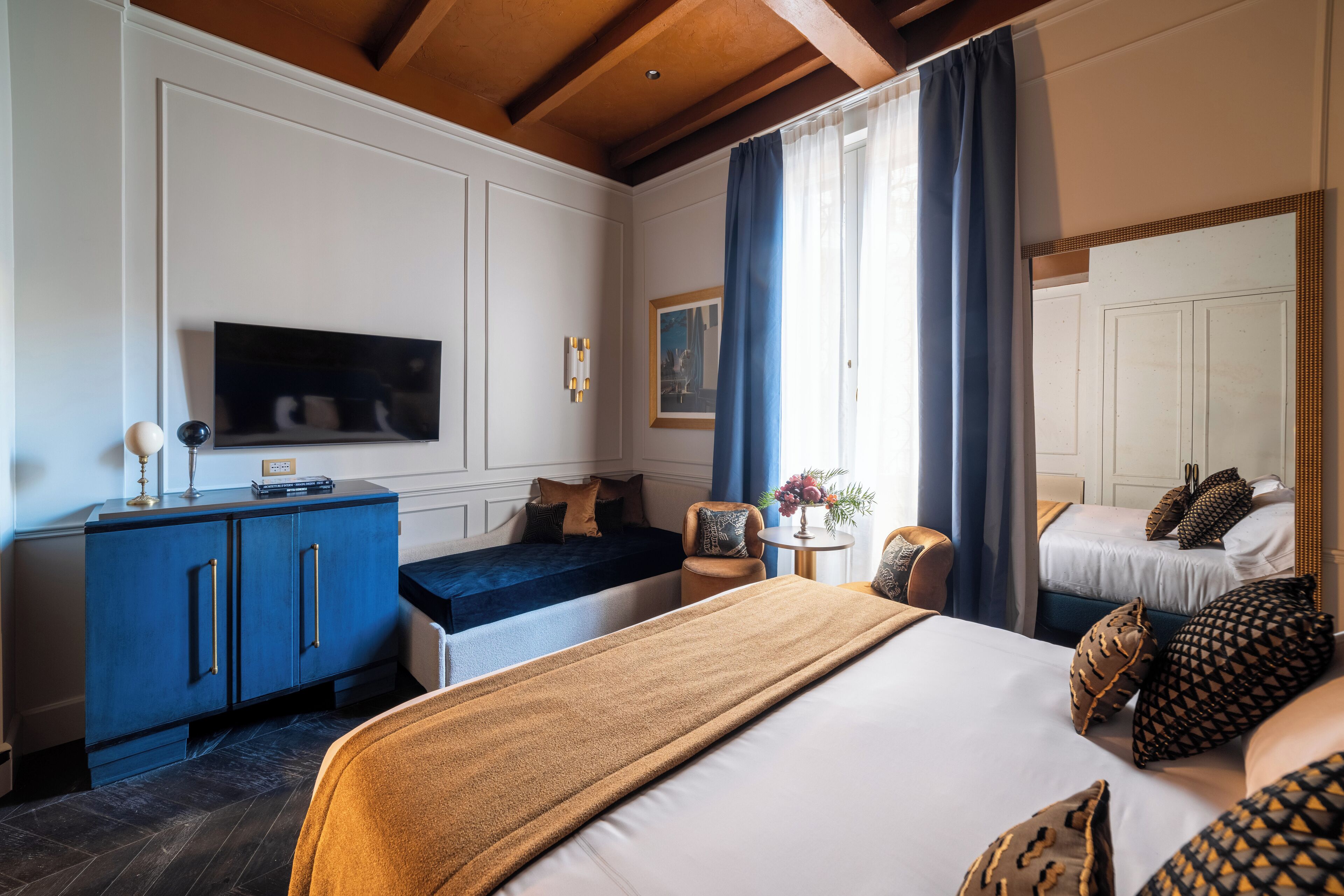 A hotel room with a bed, a sofa, a TV, a desk, and a window with curtains.