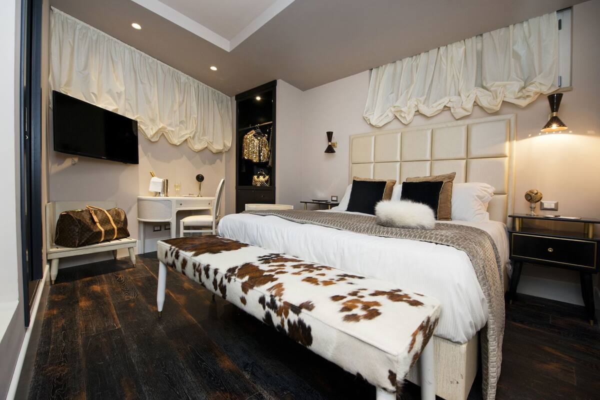 A bedroom with a large bed, a bench, a desk, a chair, and a TV.