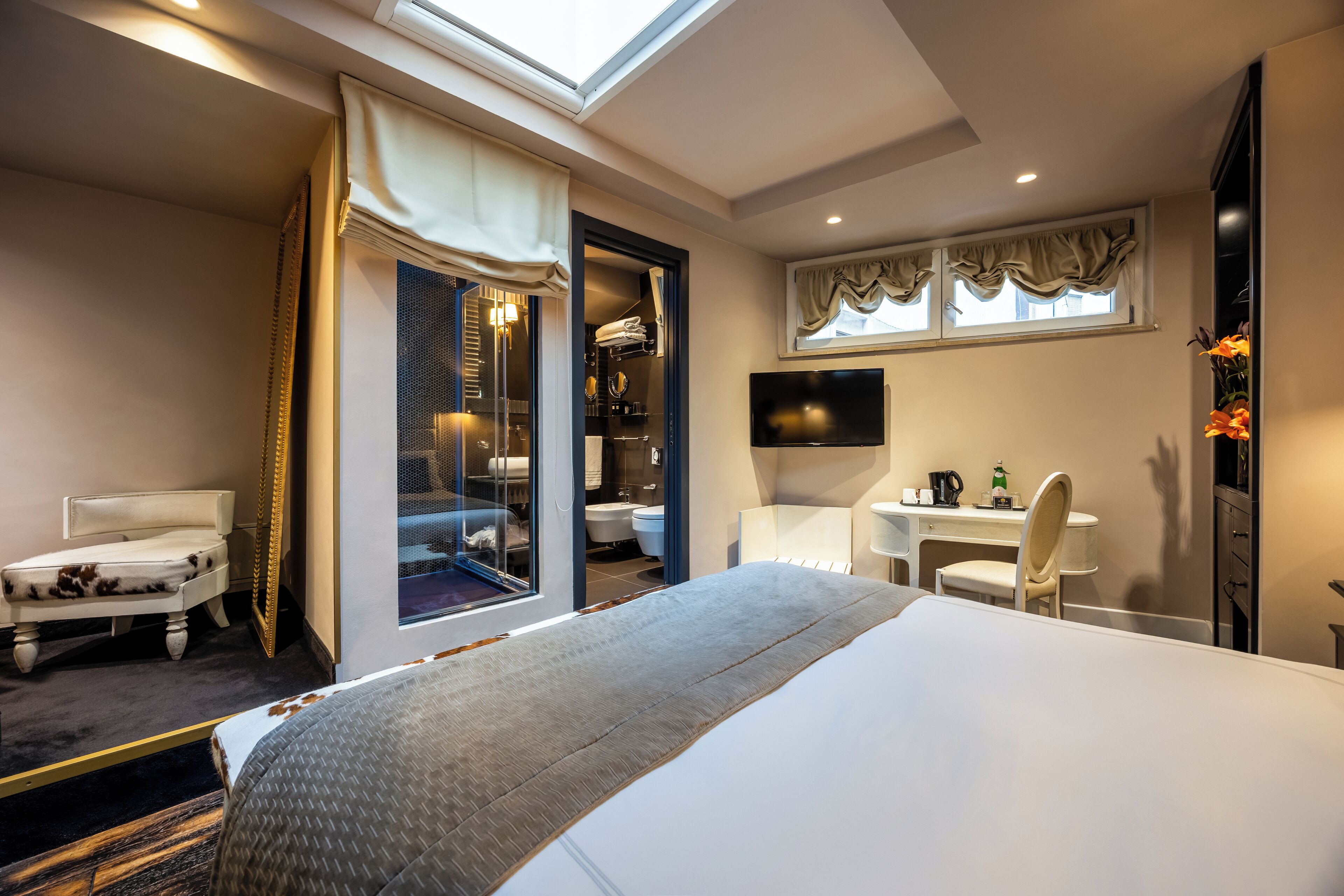 A hotel room with a large bed, a desk with a chair, a TV, and a bathroom visible through an open door.