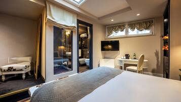 A hotel room with a large bed, a desk with a chair, a TV, and a bathroom visible through an open door.