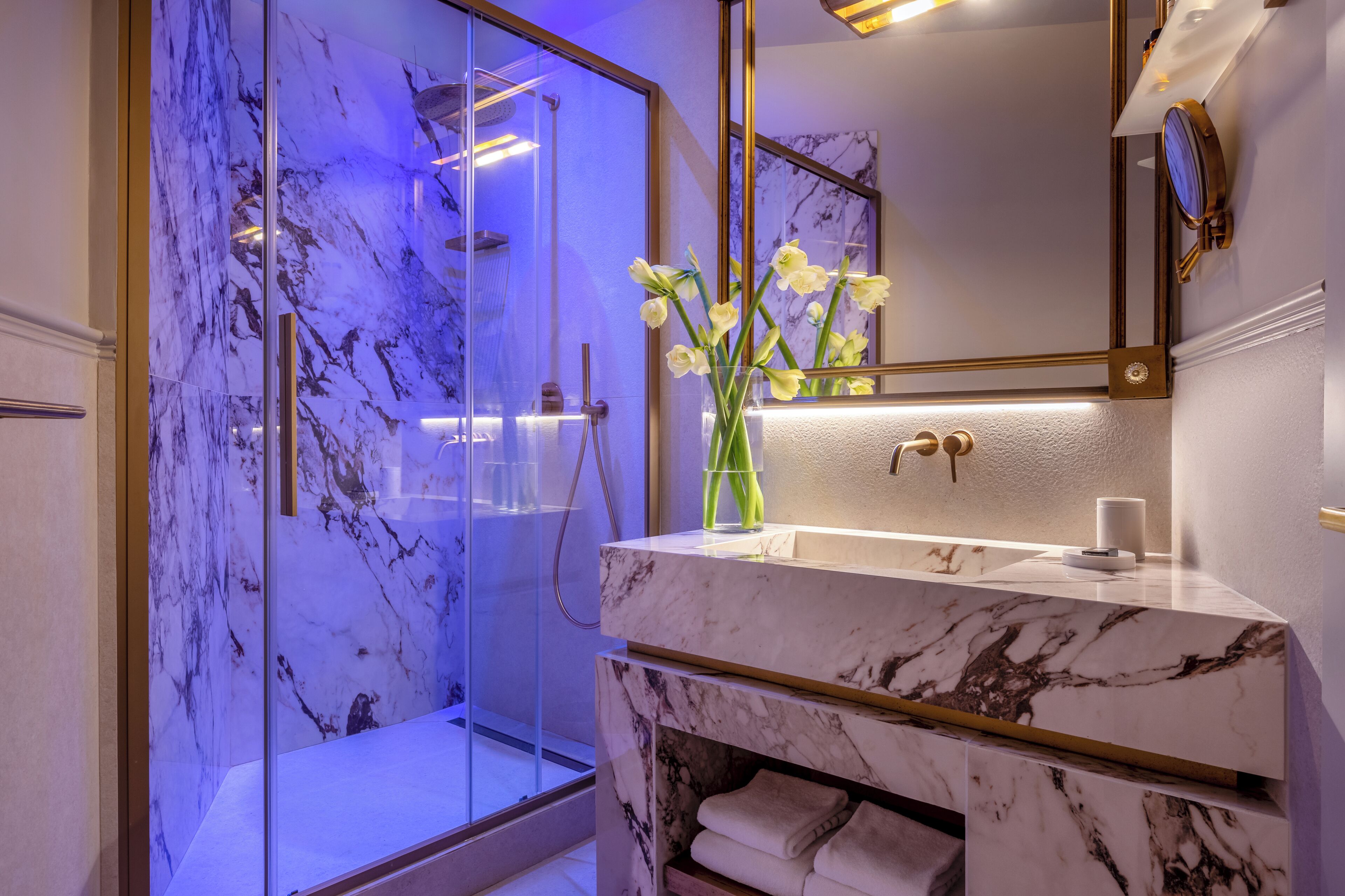 A modern bathroom with a glass-enclosed shower, marble countertops, and a vase with flowers.