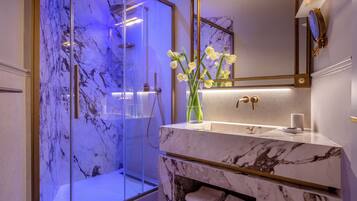 A modern bathroom with a glass-enclosed shower, marble countertops, and a vase with flowers.