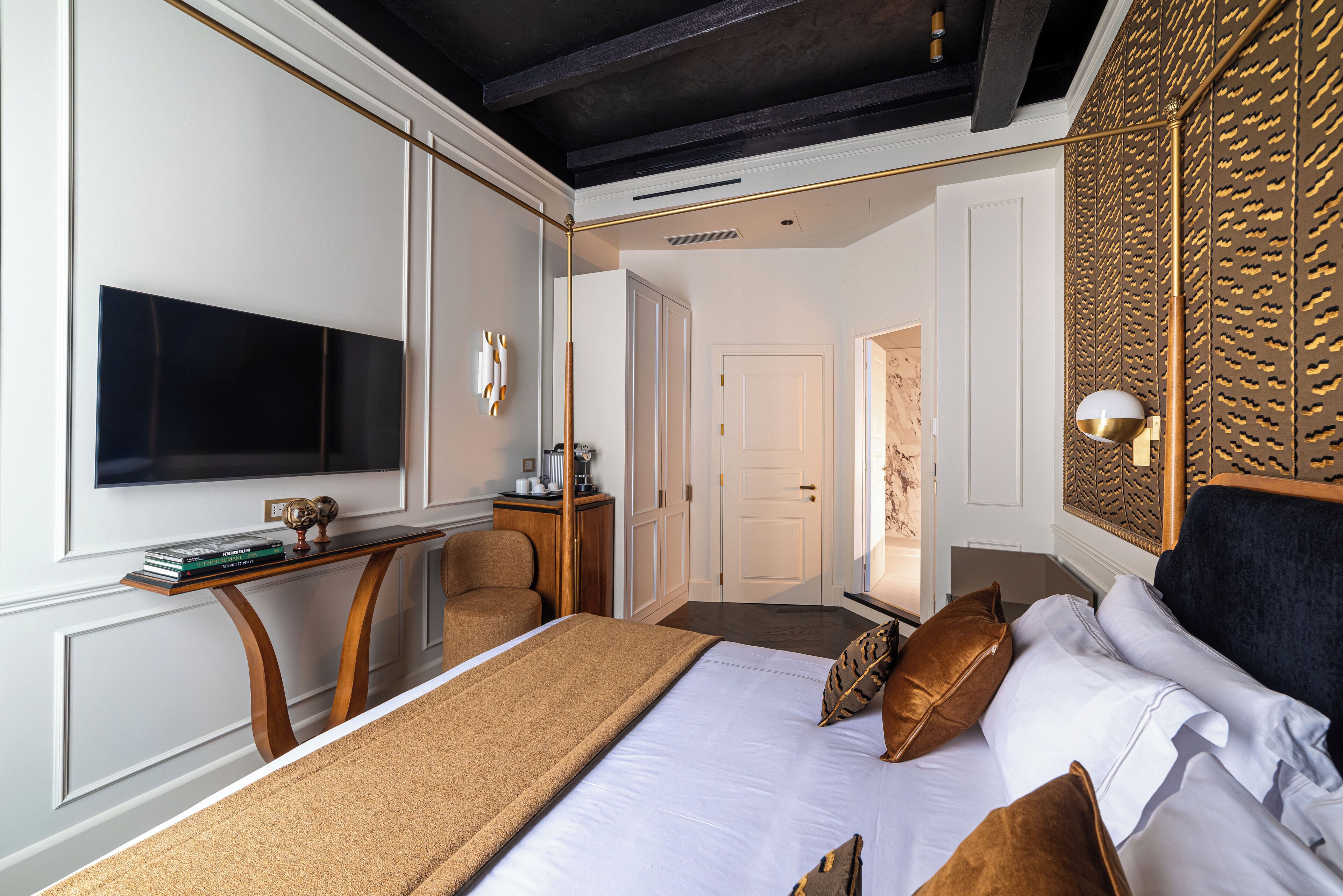 Une chambre moderne avec un grand lit, un téléviseur fixé au mur, un bureau avec une chaise et un panneau décoratif mural.