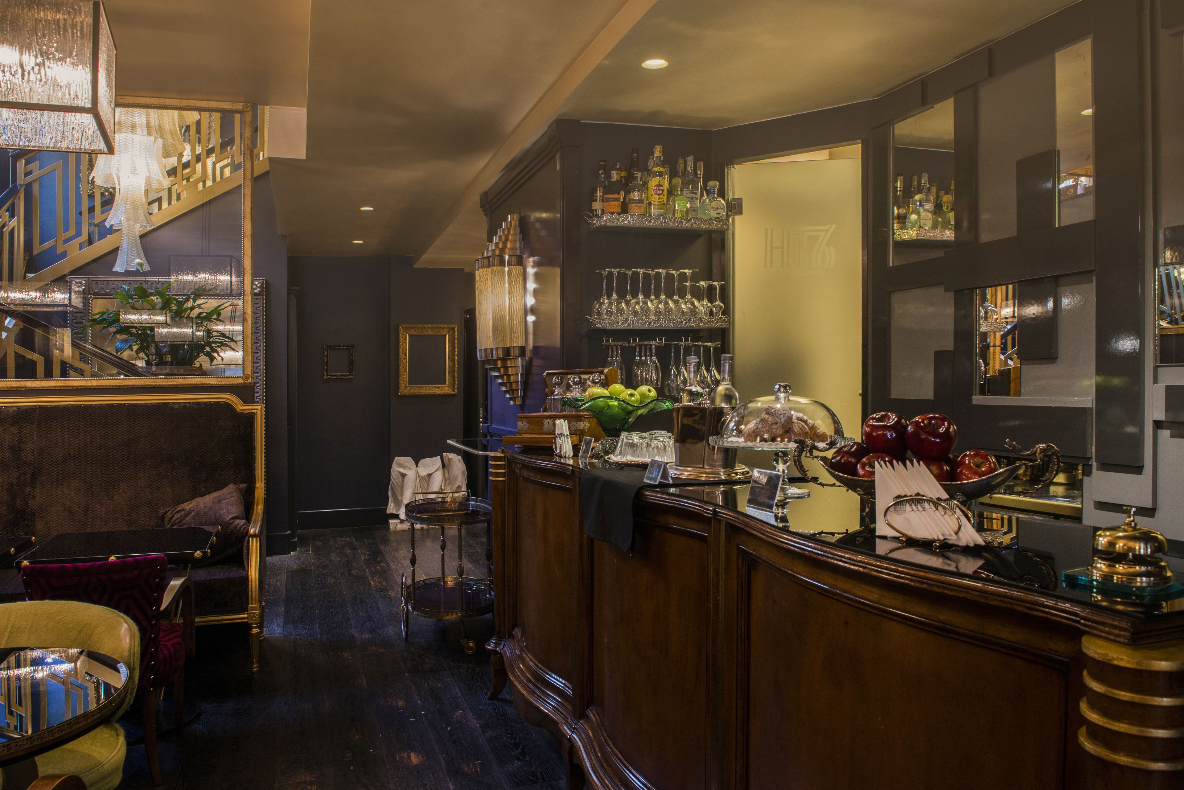 Un espace bar avec un comptoir en bois, des étagères remplies de bouteilles et de verres, et un panier de fruits.