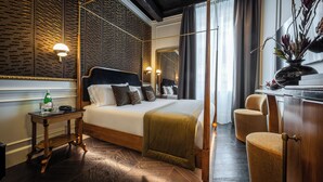 Ein modernes Hotelzimmer mit einem großen Bett, einem Nachttisch mit Flasche und Gläsern, einem Spiegel und Blick auf die Stadt durch das Fenster.