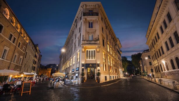 Ein historisches Gebäude mit einem zentralen Eingang, großen Fenstern und einer gepflasterten Straße davor.