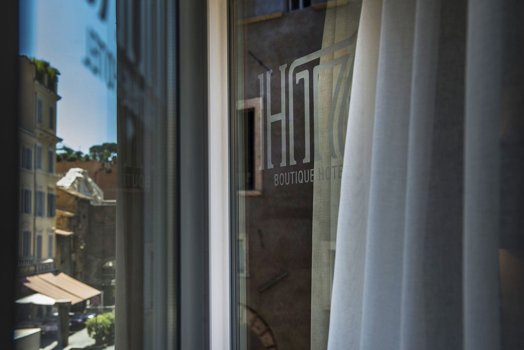 Ett fönster med en skylt som visar texten ”HOTEL BOUTIQUE HOTEL” och en utsikt över byggnader utanför.