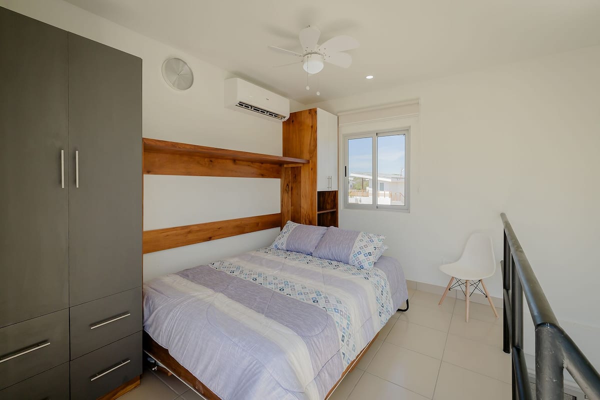 Ein Schlafzimmer mit Bett, Kleiderschrank, Deckenventilator, Fenster und einem Sessel.