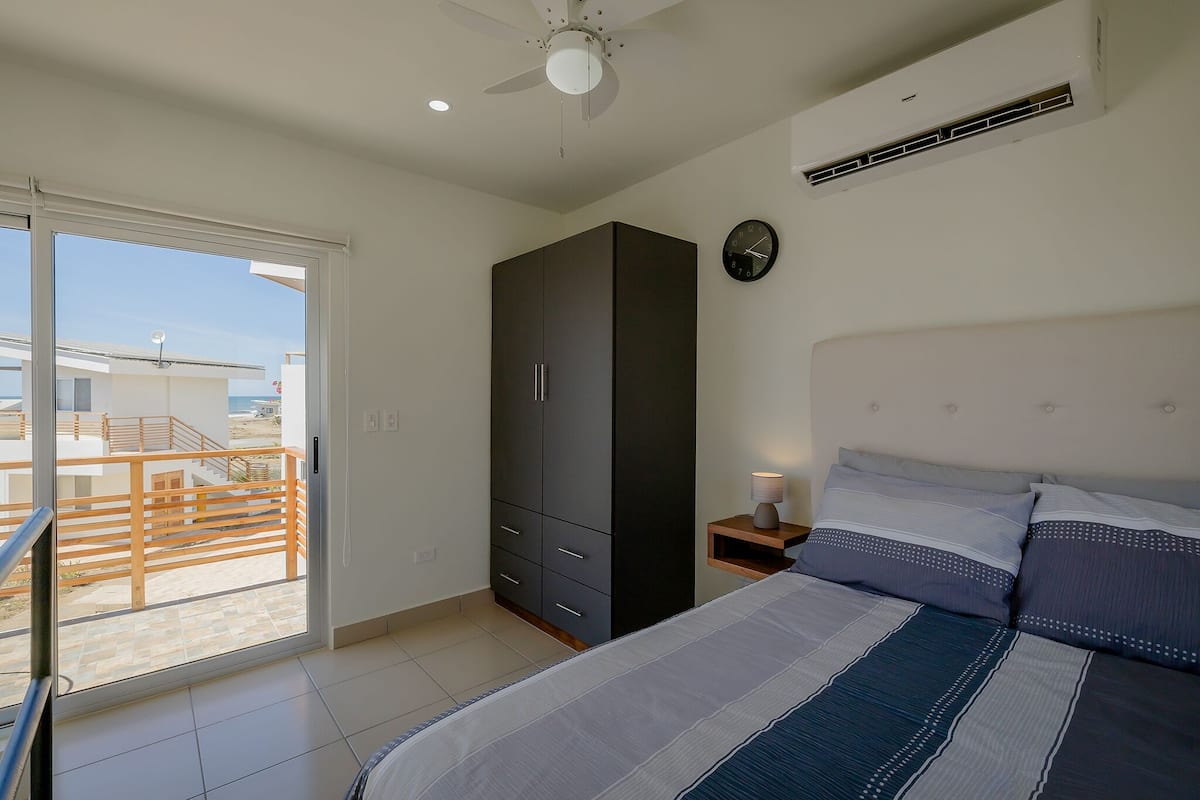 Ein Schlafzimmer mit Bett, Kleiderschrank, Nachttisch mit Lampe und Blick auf den Balkon.