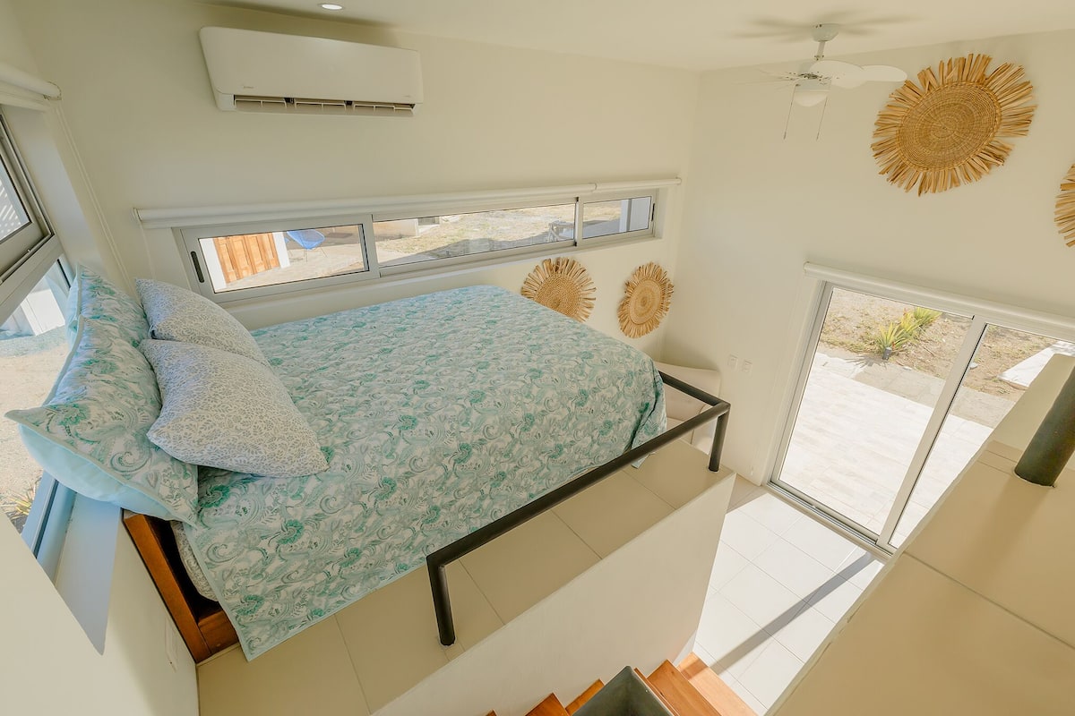 Ein Schlafzimmer mit einem Bett, Kissen, einem Fenster und einem Deckenventilator.