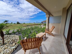 A balcony with two wooden chairs and a table, overlooking a landscaped garden and a beach. - Gran Pacifica Beach Resort & Homes (Villa El Carmen)