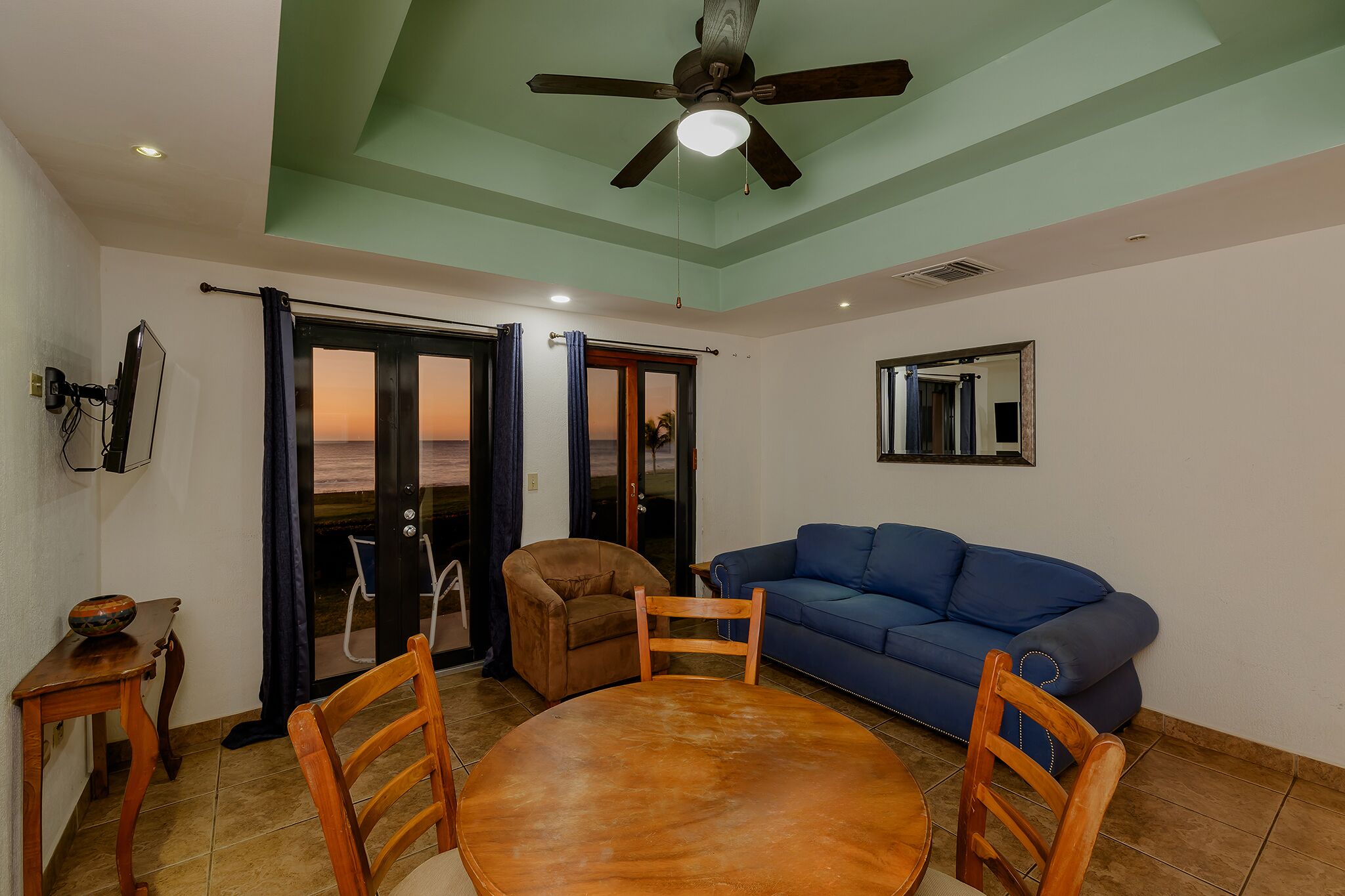 Ein Wohnzimmer mit Deckenventilator, einem blauen Sofa, einem braunen Sessel und einem Holztisch.