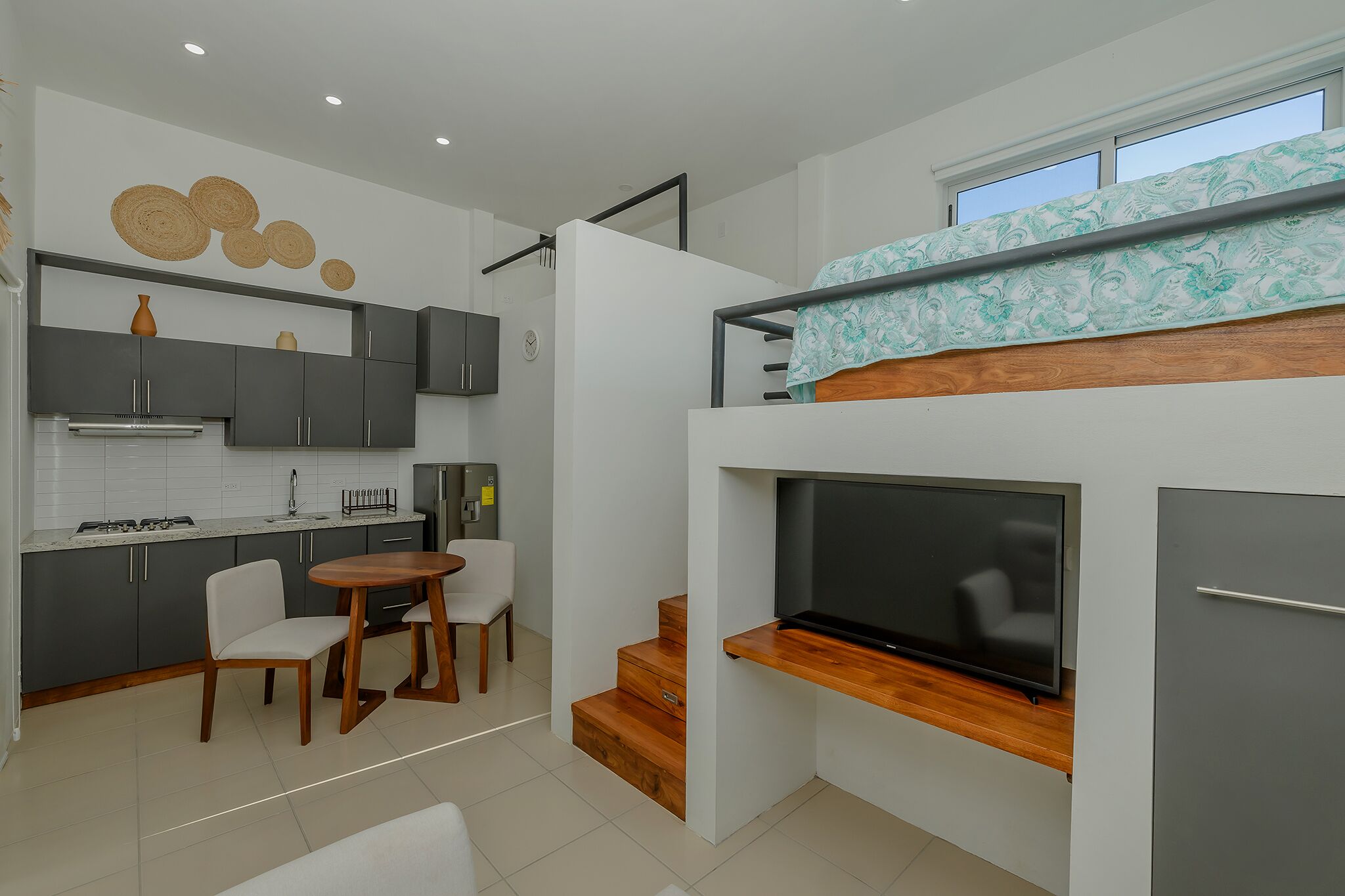 A compact living space with a kitchenette, dining area, and a TV mounted on a wall.