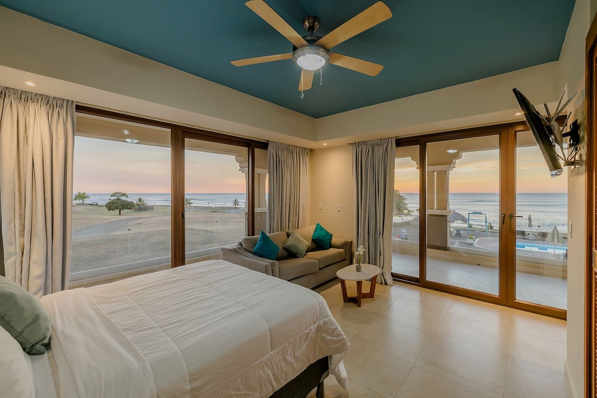 Ein Schlafzimmer mit Bett, Sofa, Deckenventilator und Blick auf den Strand.