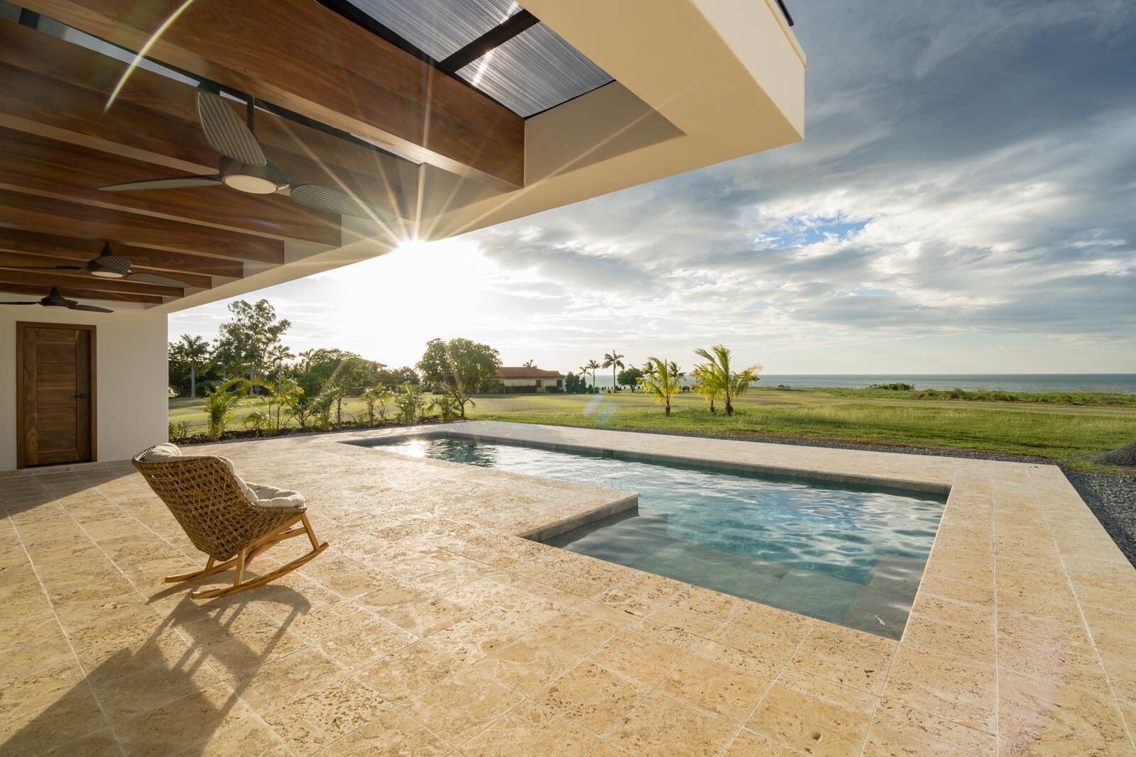 A modern outdoor pool area with a view of the ocean and a grassy landscape.