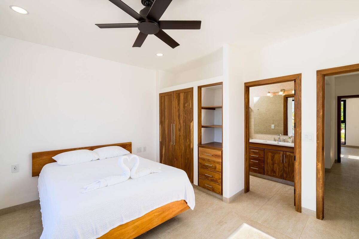 Ein Schlafzimmer mit Bett, Holzschrank und einem Badezimmer mit Spiegel und Waschbecken.