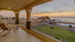 Ein Balkon mit Holzstühlen, einem Pool und Blick auf den Strand bei Sonnenuntergang.