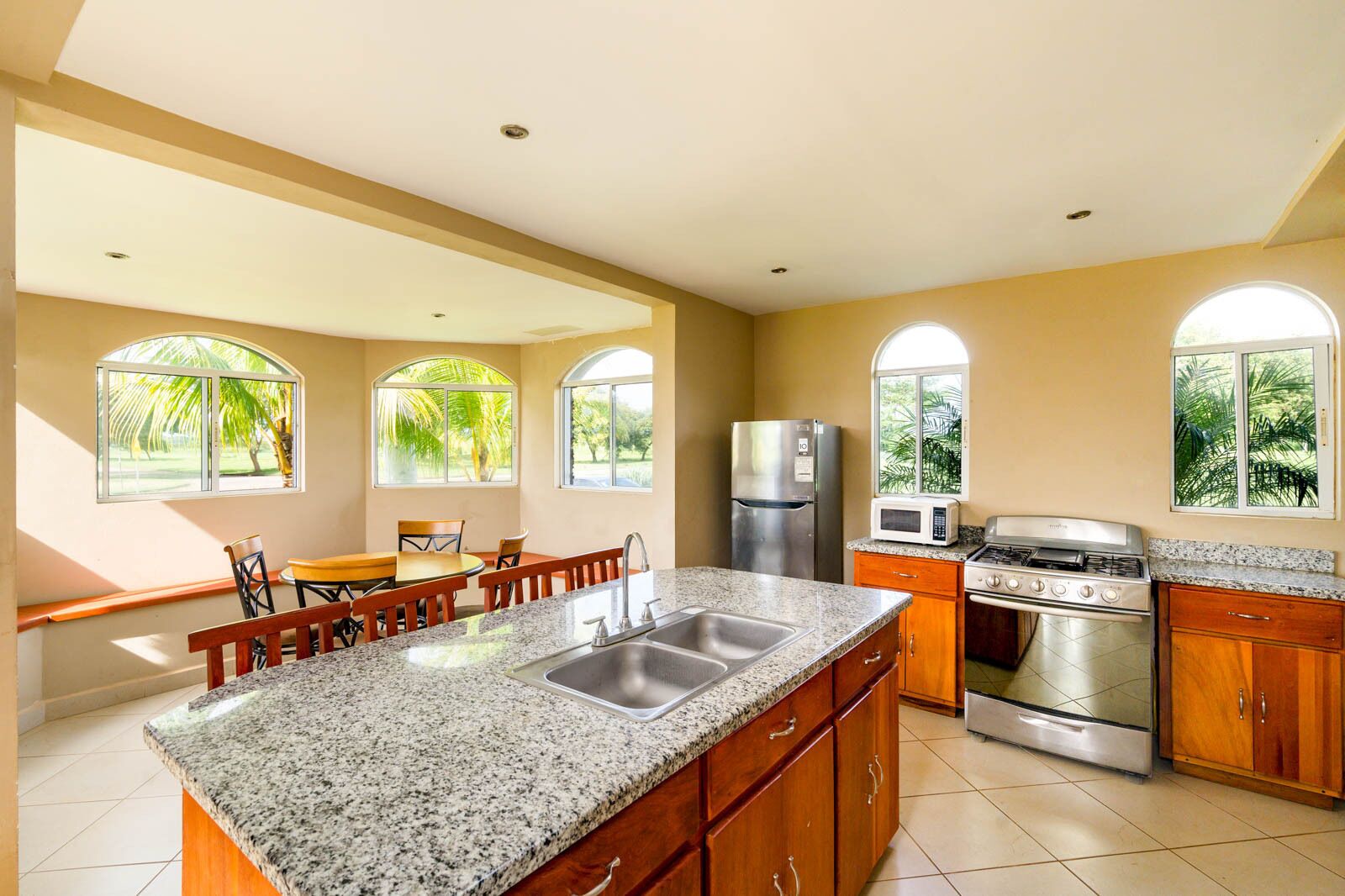A spacious kitchen with granite countertops, a central island, a refrigerator, a microwave, a stove, and wooden cabinets.