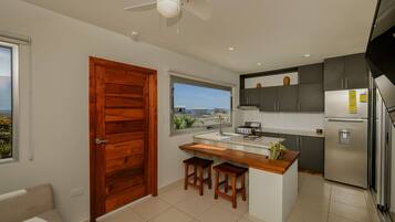 A modern kitchen with a wooden door, a window with a view, and a built-in island with stools.