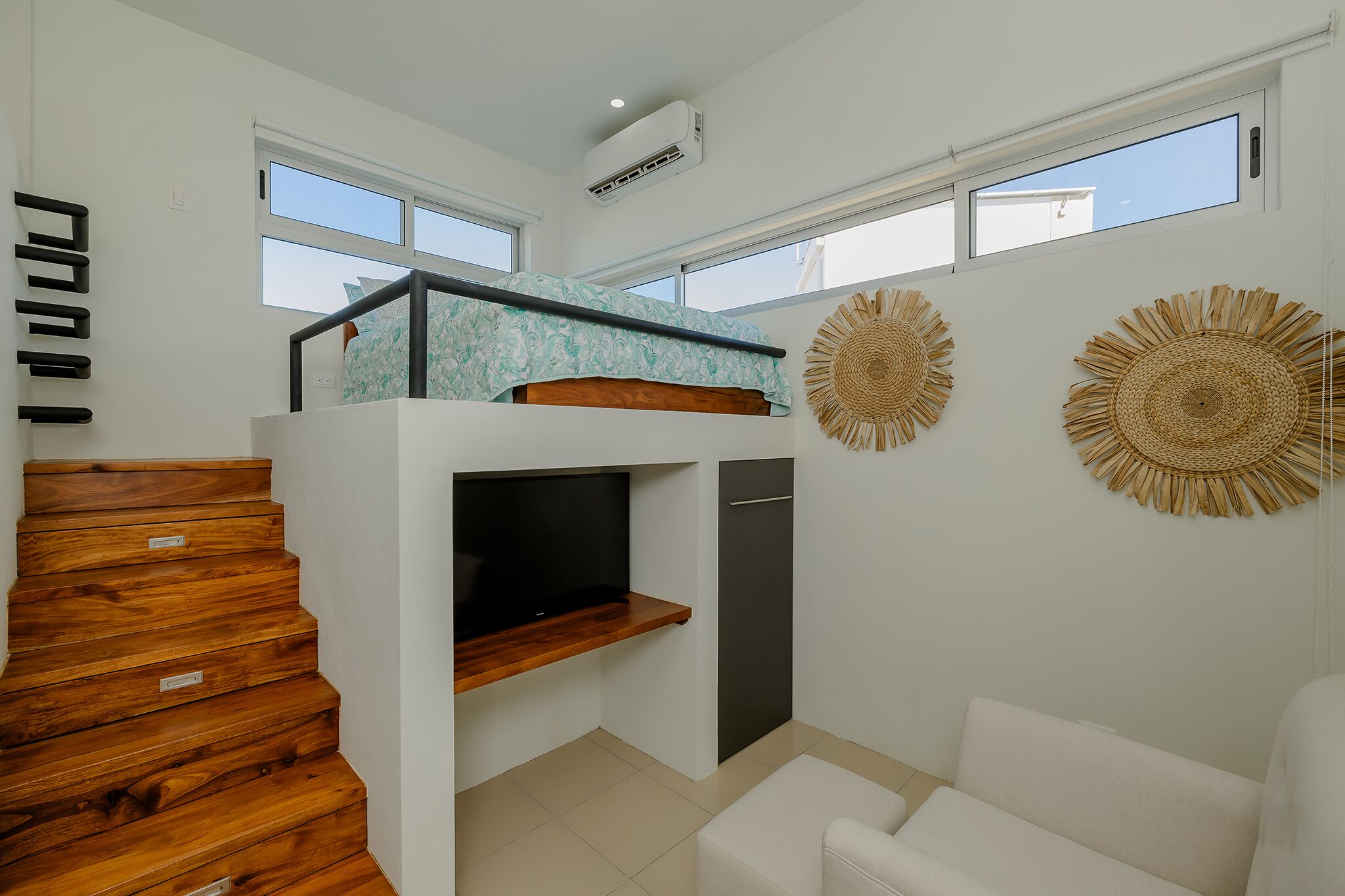 A modern interior with a wooden staircase, a bunk bed, a TV, and two large windows.