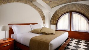 A bedroom with a bed, nightstand, lamp, and arched windows. - Roma Resort Termini (Rome)