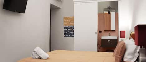 A hotel room with a bed, a television mounted on the wall, a bathroom with a mirror, sink, and towel rack.